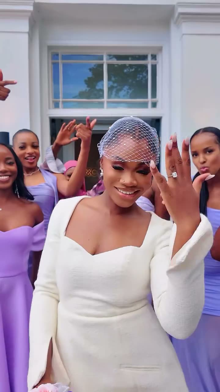 A bride-to-be in a white dress and birdcage veil with cheering bridesmaids in lilac